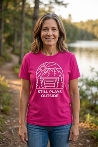 Load image into Gallery viewer, Middle-aged woman wearing the pink Still Plays Outside shirt outdoors